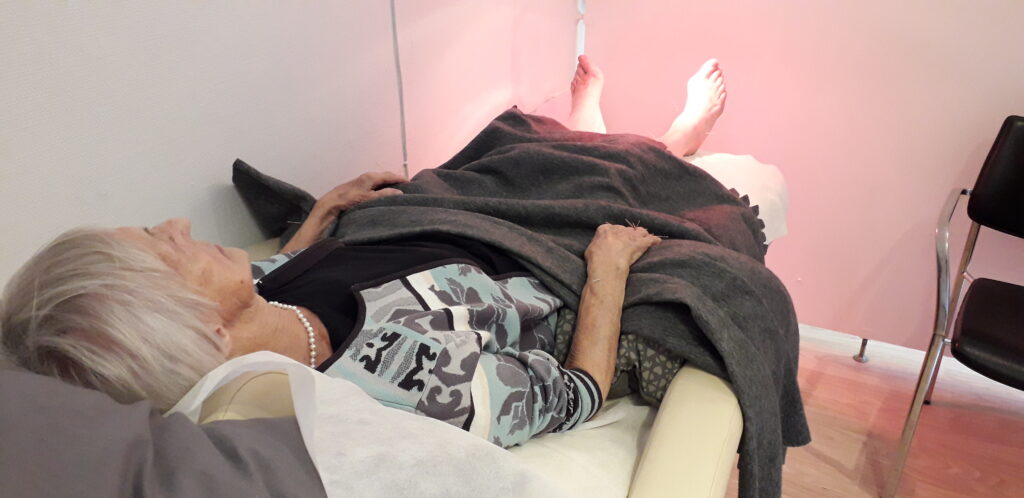 En dame der ligger i akupunktur stol med nåle i fødderne- Akupunkturbehandling