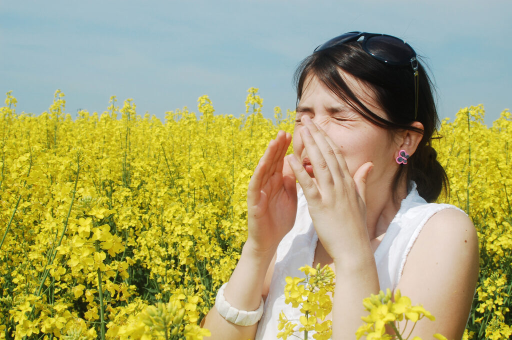 En person der nyser og har allergi i en blomstermark - Allergi